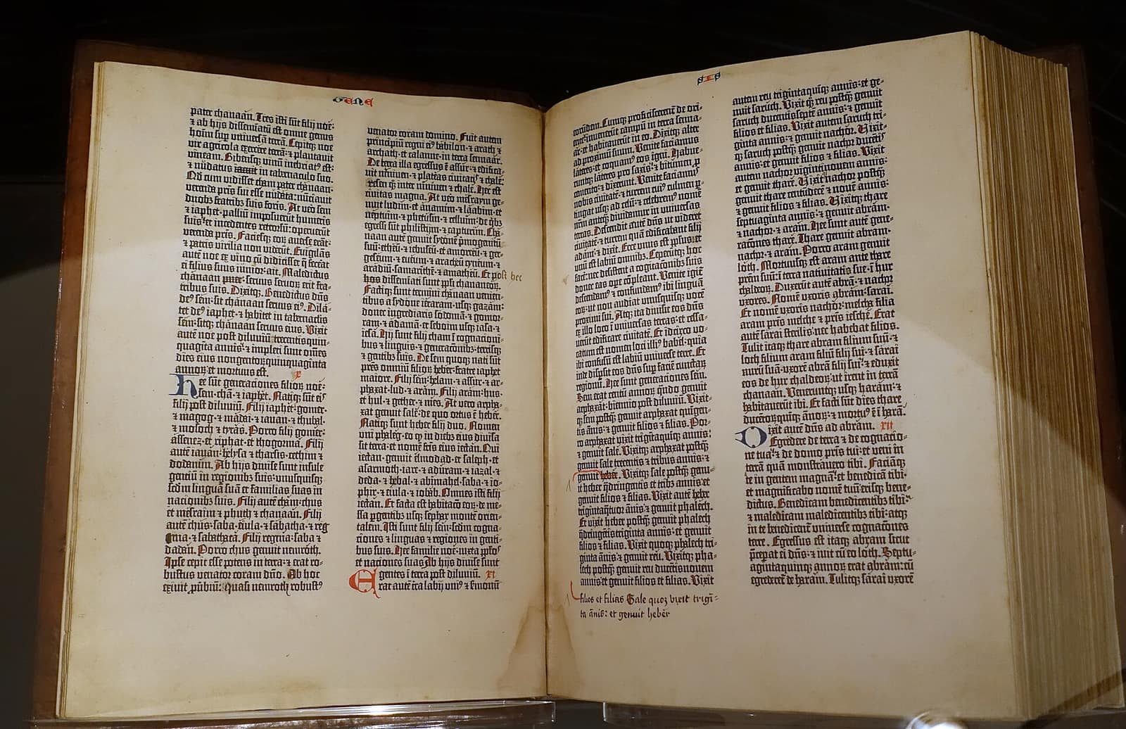 Um exemplar da Bíblia de Gutenberg aberto sobre um suporte, com duas páginas de texto em duas colunas e letras iniciais coloridas à mão