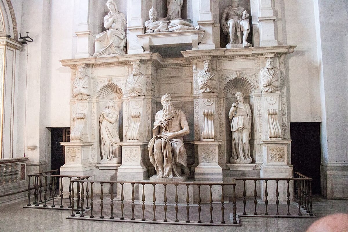 Estátua de mármore de Moisés sentado, barbudo, com tábuas sob o braço e dois pequenos chifres na testa