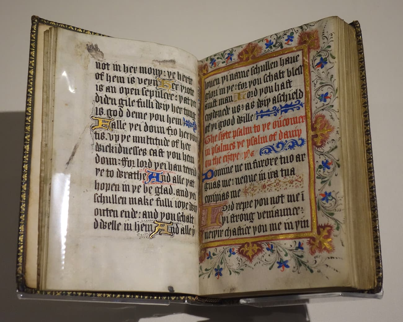 Livro aberto: um saltério com texto em letra gótica, em inglês, e uma página com moldura dourada e floral, com o título do Salmo 6 em vermelho