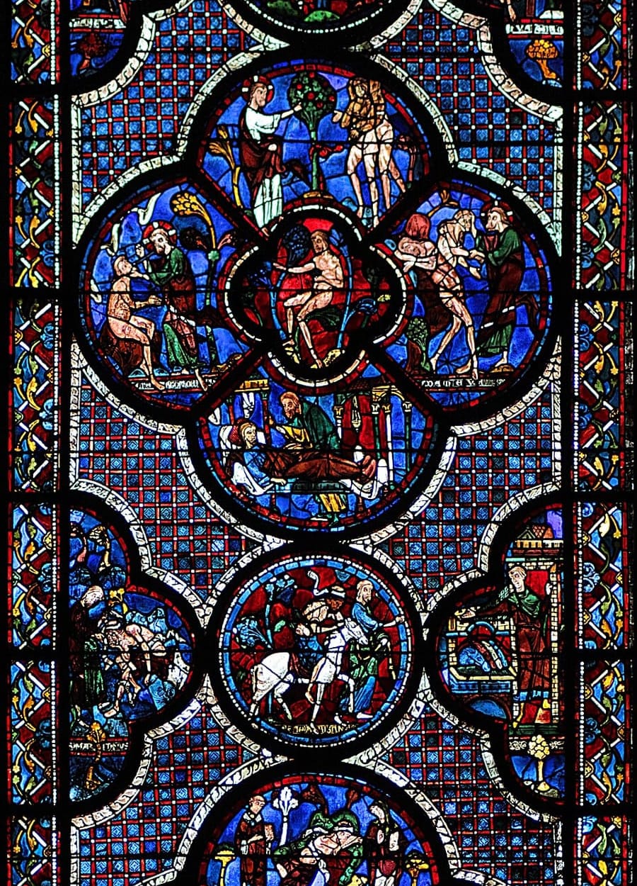 Vitral azul e vermelho com medalhões circulares: cenas de Adão e Eva em volta de um medalhão central, e abaixo o samaritano a cavalo com o homem ferido