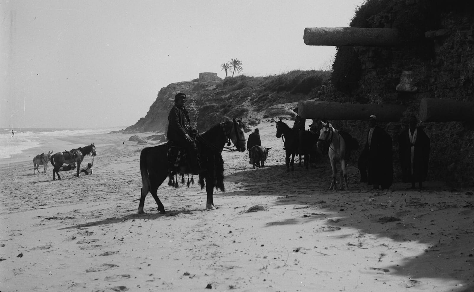 Fotografia antiga de ruínas de Ascalom à beira-mar, com cavaleiros e colunas de pedra encravadas na encosta